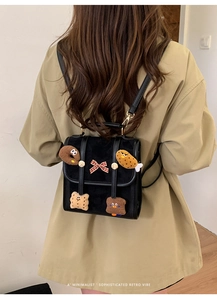Detail view of a retro black mini backpack featuring plush badges and a red checkered bow