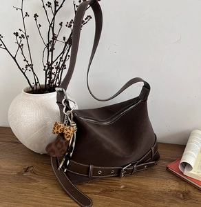 Detail of dark brown leather tote bag with a leopard bow and heart charm on a wooden table