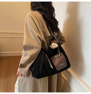 Detail of black suede tote bag with brown leather pocket and cute plush bear keychain