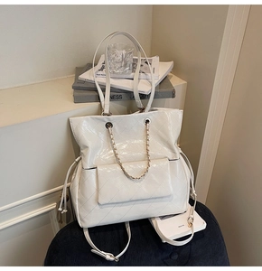 Detail of white quilted tote bag featuring chain straps and side drawstring on a stool