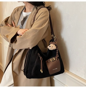 Detail of large black suede tote bag with brown leather straps and plush puppy charm