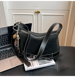 Close-up of black leather tote with white contrast stitching and heart-shaped metal charm