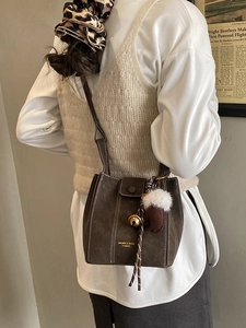 Brown suede bucket bag with contrast stitching and charms shown in a lifestyle view