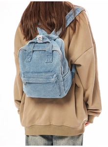 Nahaufnahme des hellblauen Denim-Rucksacks mit Tragegriff und Reißverschlusstasche am Rücken