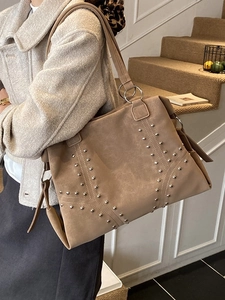 Grand sac cabas kaki clouté en daim mat porté par un mannequin dans un décor d'escalier