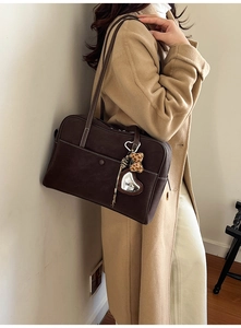Detail of dark brown tote bag with white stitching, plush bear and heart charms