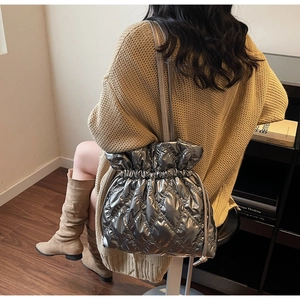 Detail view of silver metallic quilted bucket bag with drawstring closure on model