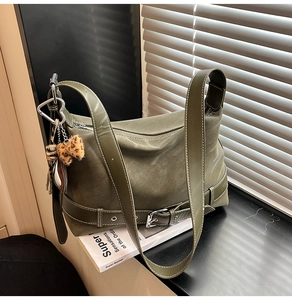 Detail of olive green suede tote bag with decorative belt buckles and leopard bow charm