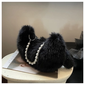 Détail d'un sac à main en peluche noire avec chaîne en perles sur socle blanc