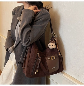 Detail of a large brown suede tote bag with decorative bear pendant and silk scarf