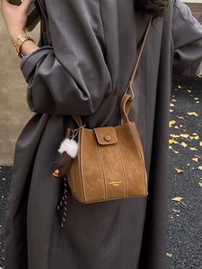 Brown matte suede bucket bag with white contrast stitching and tassel charm in autumn