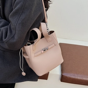 Detail of light pink bucket bag with leather texture and twist-lock on grey coat