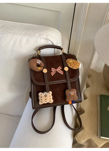 Detail of dark brown vintage backpack featuring plush cookie patches and red bow accent