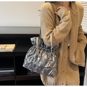 Close-up of quilted silver bucket bag with drawstring closure and metallic chain strap