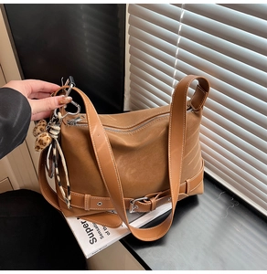 Detail of tan suede tote bag with decorative buckles and leopard print pompom charm
