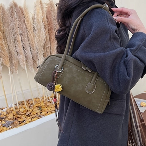 Dettaglio borsa in pelle verde oliva con nappina boho su supporto di marmo