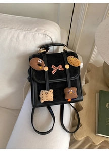 Close-up of black suede backpack with cartoon plush patches on a cozy white sofa