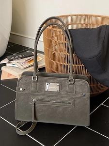 Deep grey frosted suede tote bag with front zipper and metal nameplate shown in a cozy setting