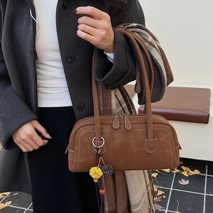 Dettaglio della borsa Boston in pelle marrone vintage con ciondolo e outfit autunnale