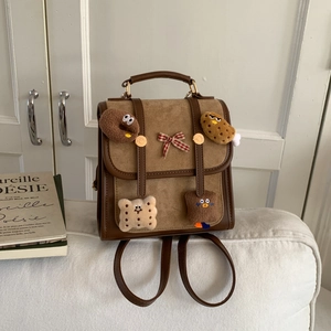 Detail showing retro brown small backpack with plush charms and bow on fabric background