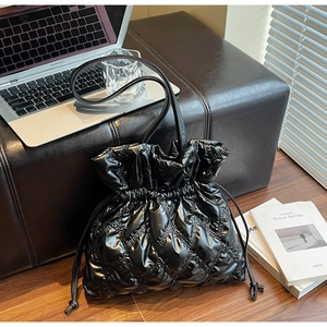 Detail of black quilted puffer bucket bag with drawstring closure in a modern office setting