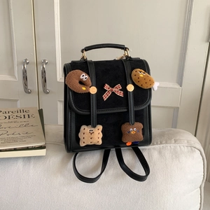 Detail of a black suede backpack with cute cartoon plush patches and red checkered bow