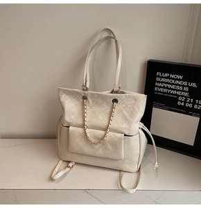 Detail of white quilted tote bag featuring chain magnetic flap pocket and drawstrings