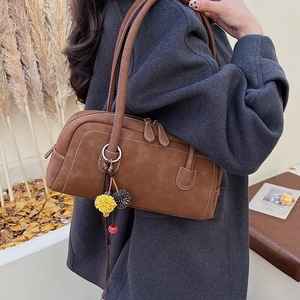 Dettaglio della borsa bowling in pelle marrone con cuciture bianche e pompon decorativi
