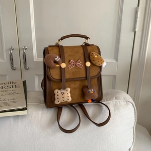 Brown suede backpack with cookie patches and bow on a white sofa with magazine