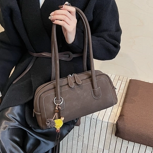 Dettaglio borsa bowling in pelle marrone con doppia zip e ciondolo a pompon