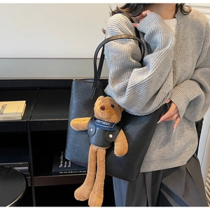 Detail der schwarzen Leder-Einkaufstasche mit süßem Teddybär-Anhänger und blauem Schal