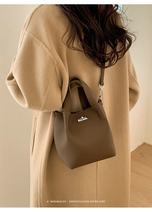 Deep brown pebble leather bucket bag with silver metal lock on a camel wool coat