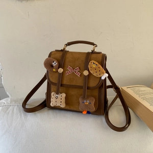 Close-up of brown suede backpack with cute plush food charms and red checkered bow detail