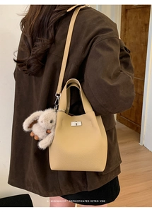 Detail of beige pebbled leather bucket bag with silver lock and plush rabbit charm