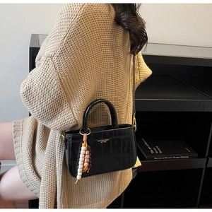 Detalle de bolso negro con textura de cocodrilo con letras doradas y cuentas decorativas
