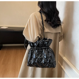 Detail of black glossy quilted bucket bag with drawstring closure and slim shoulder strap
