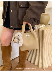 Detail of beige leather bucket bag featuring a silver twist lock and plush rabbit charm