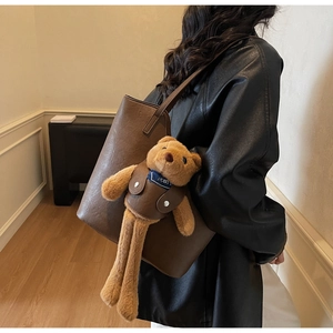 Detail einer großen dunkelbraunen Leder-Tote-Bag mit Plüschbären-Anhänger an einem Model