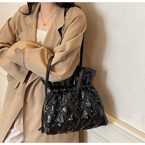 Close-up of a black quilted bucket bag with drawstring closure on a model wearing a trench coat