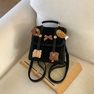 Detail of black leather bag featuring cute plush food charms and checkered bow on book