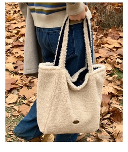 Dettaglio borsa tote in pile color crema con manici blu navy su terreno boschivo