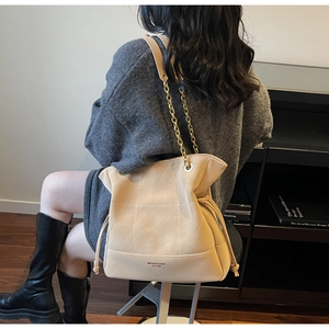 Detail of beige bucket bag featuring matte texture and elegant metal chain strap