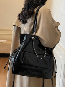 Quilted black patent leather shoulder bag with metal chain strap worn on a beige coat