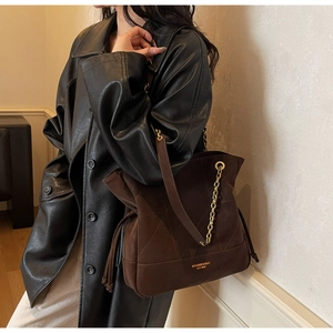 Detail of dark brown tote with quilted stitching, gold chain strap, and tassel accents