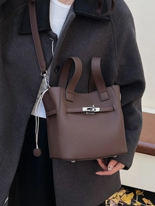 Brown lychee leather bucket bag with metal turn-lock closure shown in a winter setting