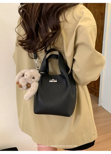 Detail view of a black bucket bag with silver clasp and plush rabbit charm on a model