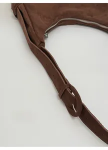 Detail of wide adjustable suede shoulder strap with silver buckle on brown hobo bag