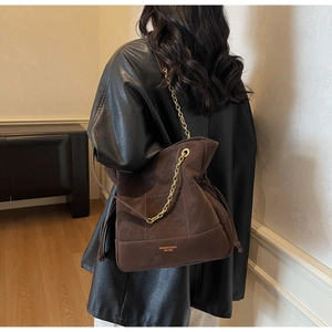 Detail of dark brown quilted suede bucket bag featuring golden chain and brand logo