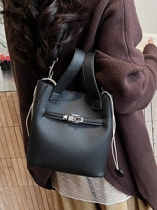 Elegant black pebble leather bucket bag with silver clasp shown on shoulder over brown sweater