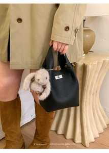 Detail of black pebbled leather bucket bag with silver clasp and plush rabbit charm